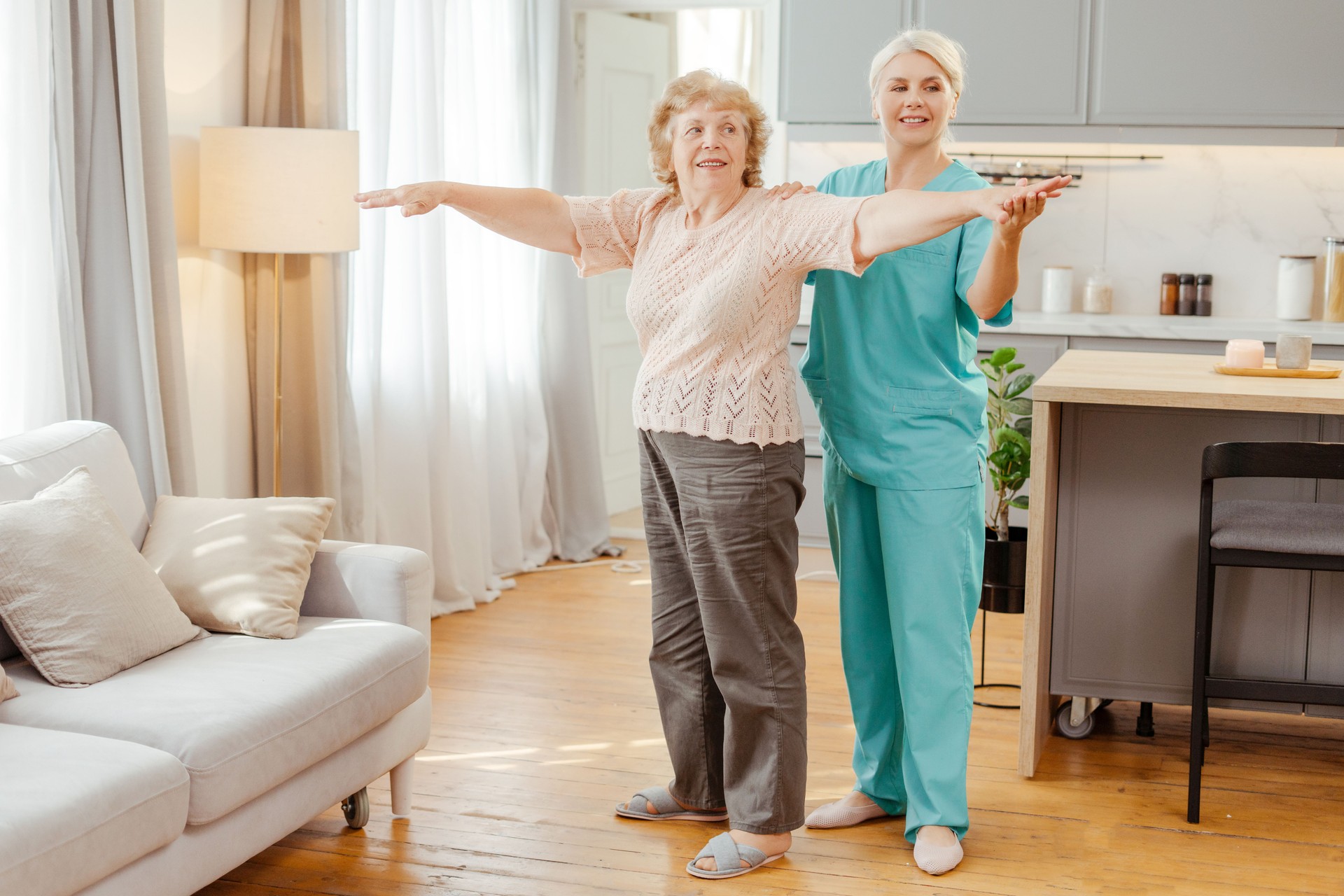 Smiling nurse assisting happy senior woman doing rehabilitation exercises at home